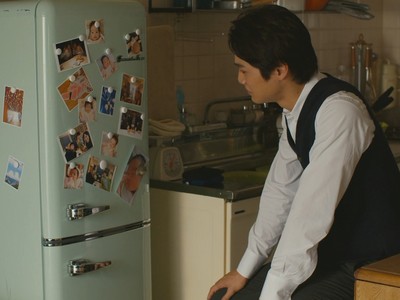 Eiji looks wistfully at the pictures of his daughter and wife on the fridge.